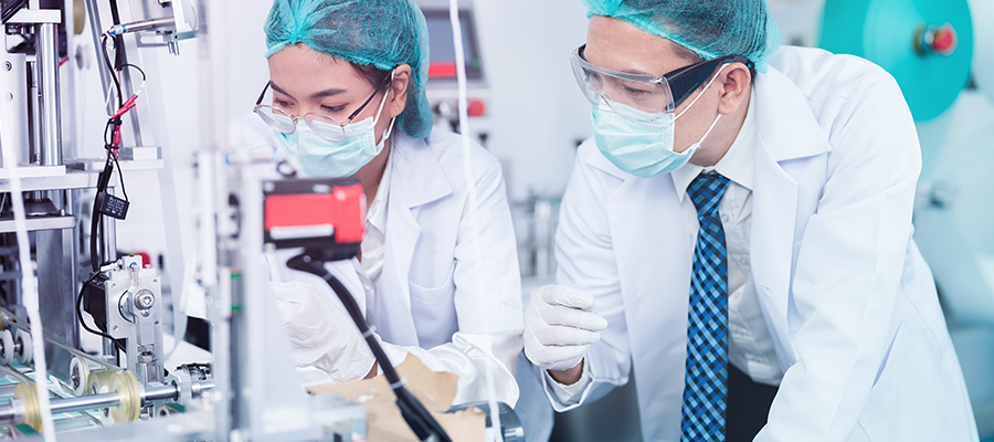 Medical device scientists outfitted with protective gear and examining the eQMS process.