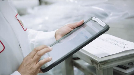 Person in a lab coat using a tablet in a factory